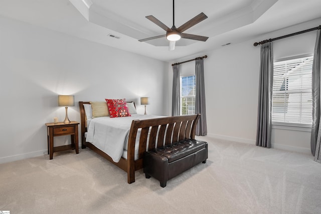 bedroom with visible vents, light colored carpet, and a tray ceiling