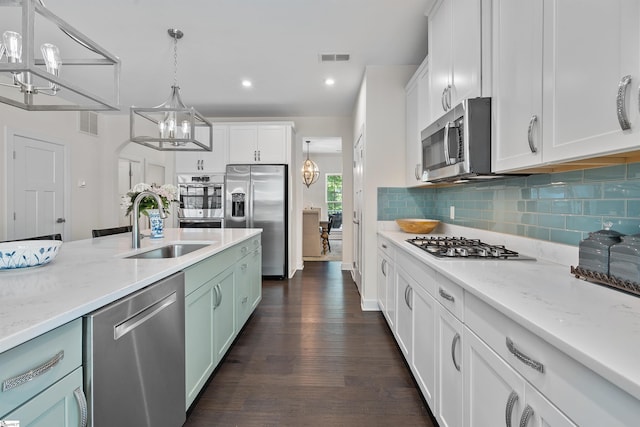 kitchen featuring a sink, decorative backsplash, appliances with stainless steel finishes, white cabinets, and a notable chandelier