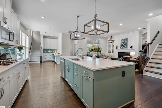 kitchen with dark wood-style floors, a sink, an inviting chandelier, white cabinetry, and appliances with stainless steel finishes
