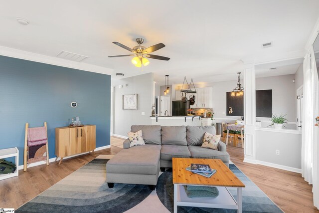 living room featuring baseboards, a ceiling fan, visible vents, and light wood finished floors