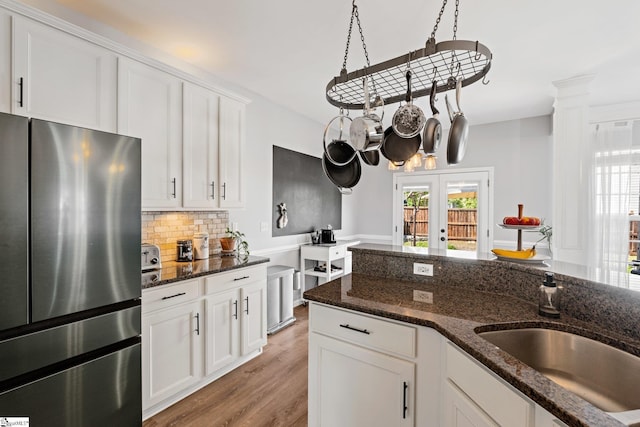 kitchen with a sink, light wood finished floors, white cabinets, backsplash, and freestanding refrigerator