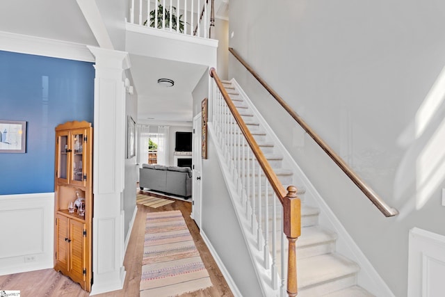 staircase featuring ornamental molding, a wainscoted wall, wood finished floors, and ornate columns