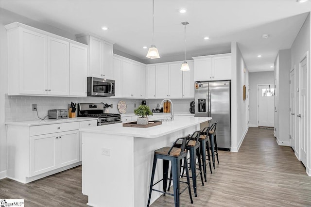 kitchen featuring light wood-type flooring, decorative backsplash, appliances with stainless steel finishes, and a center island with sink