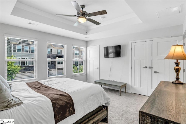 bedroom with light carpet, visible vents, ceiling fan, multiple closets, and a raised ceiling
