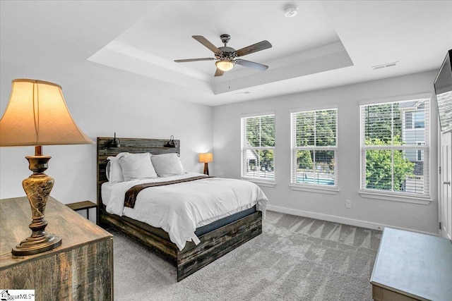carpeted bedroom featuring ceiling fan, baseboards, a tray ceiling, and visible vents