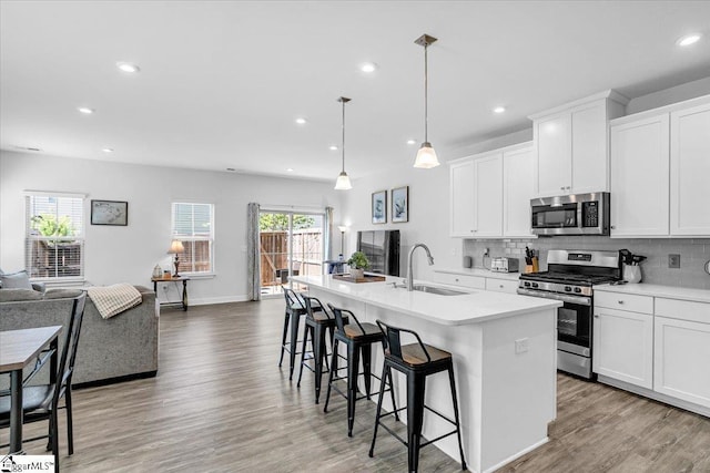 kitchen featuring a sink, open floor plan, a kitchen island with sink, stainless steel appliances, and light countertops