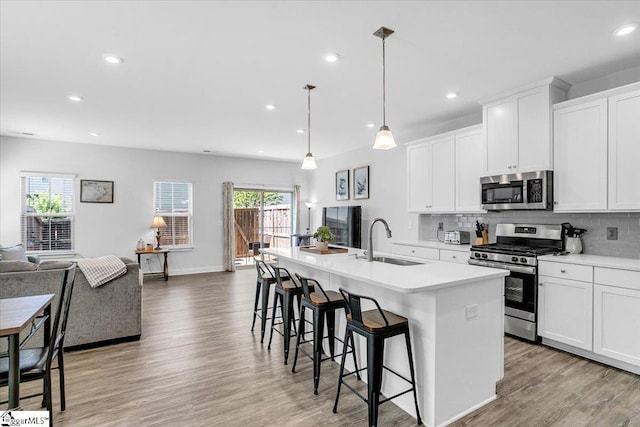 kitchen featuring an island with sink, a sink, light wood-style flooring, appliances with stainless steel finishes, and open floor plan