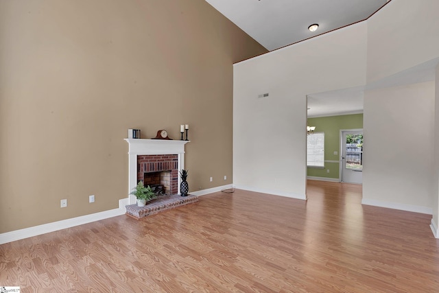 unfurnished living room with light wood-type flooring, a fireplace, baseboards, a notable chandelier, and visible vents