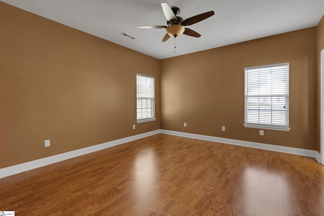 unfurnished room featuring a ceiling fan, wood finished floors, a textured ceiling, baseboards, and visible vents