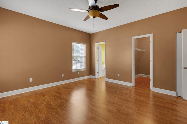 unfurnished bedroom with light wood-type flooring, baseboards, a spacious closet, a closet, and ceiling fan