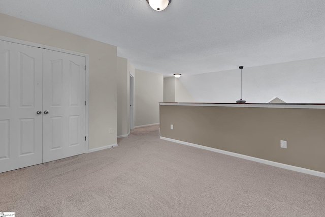 empty room featuring a textured ceiling, baseboards, and light carpet