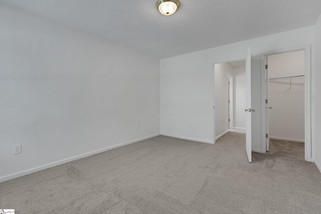 unfurnished bedroom with carpet flooring, a textured ceiling, baseboards, a closet, and a walk in closet
