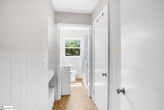 bathroom featuring tile walls, toilet, and wainscoting
