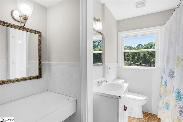 full bath with toilet, tile walls, wainscoting, visible vents, and vanity