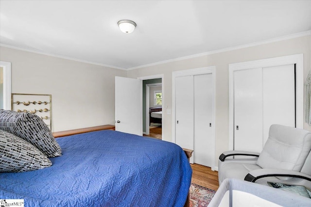 bedroom featuring baseboards, wood finished floors, two closets, and ornamental molding