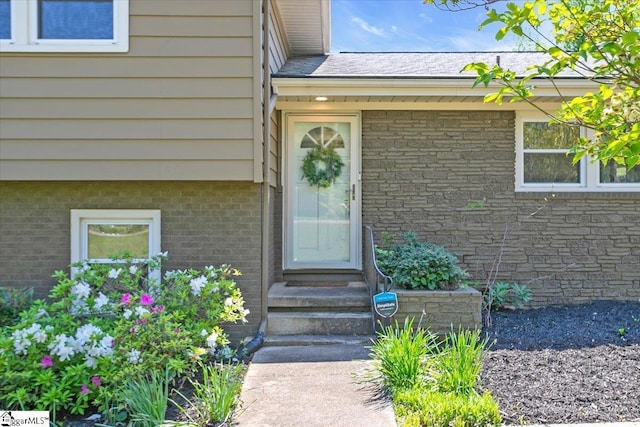 entrance to property featuring roof with shingles and brick siding