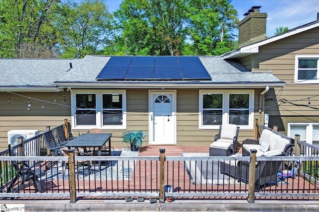 back of house featuring solar panels, central AC, a chimney, a shingled roof, and outdoor dining space