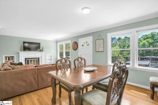 dining room with light wood-type flooring, baseboards, a glass covered fireplace, and crown molding