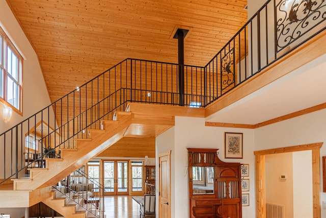 staircase featuring visible vents, wooden ceiling, a high ceiling, and a healthy amount of sunlight