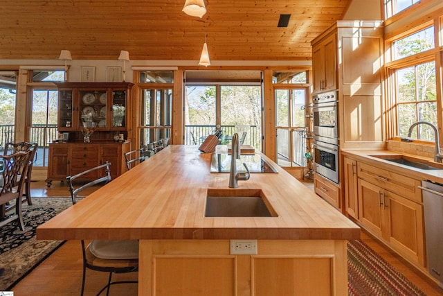 kitchen with a sink, wooden counters, a kitchen island with sink, wood ceiling, and appliances with stainless steel finishes