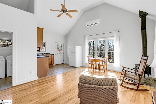 living area featuring washing machine and clothes dryer, light wood finished floors, a wall mounted air conditioner, a ceiling fan, and high vaulted ceiling