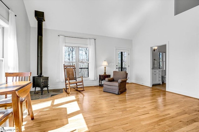 living area with light wood-style flooring, baseboards, high vaulted ceiling, and a wood stove