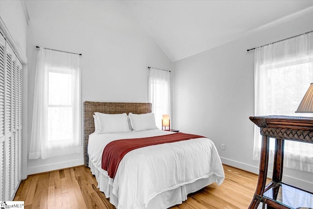 bedroom with hardwood / wood-style floors, vaulted ceiling, baseboards, and multiple windows