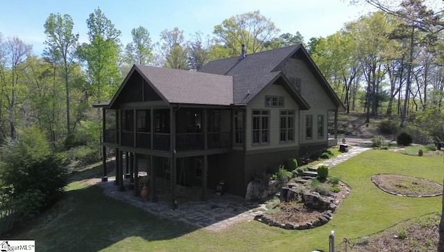 back of property featuring a yard, a sunroom, and roof with shingles