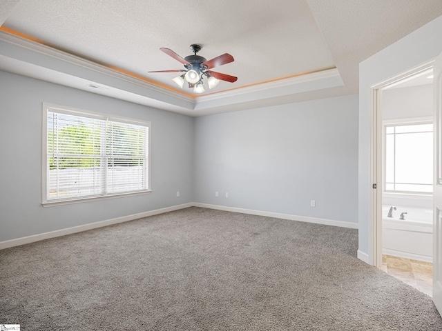 spare room with a raised ceiling, baseboards, light colored carpet, and ceiling fan