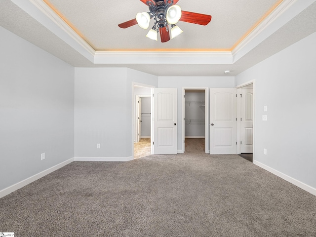 unfurnished bedroom featuring a tray ceiling, baseboards, a spacious closet, carpet, and ornamental molding