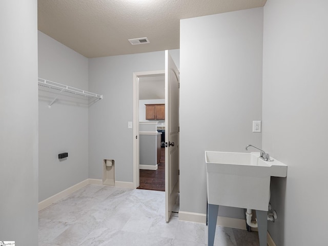washroom with baseboards, laundry area, a textured ceiling, and visible vents