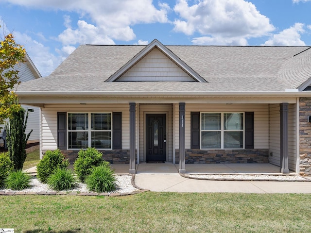 view of front of house featuring stone siding, a shingled roof, a front lawn, and covered porch