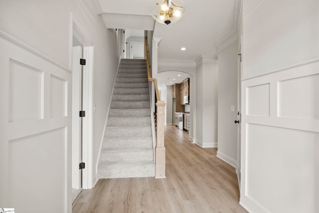 stairs featuring crown molding, wood finished floors, arched walkways, baseboards, and recessed lighting