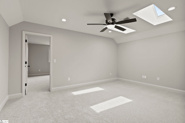 unfurnished room featuring a ceiling fan, baseboards, vaulted ceiling with skylight, and carpet