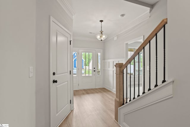 entryway featuring stairs, crown molding, light wood-style floors, and an inviting chandelier