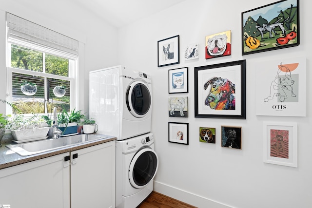 laundry area with wood finished floors, a sink, cabinet space, baseboards, and stacked washer and clothes dryer
