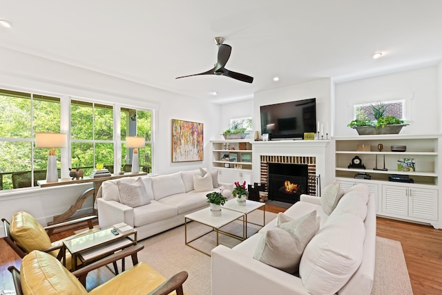 living room featuring a ceiling fan, a brick fireplace, recessed lighting, and light wood-style flooring