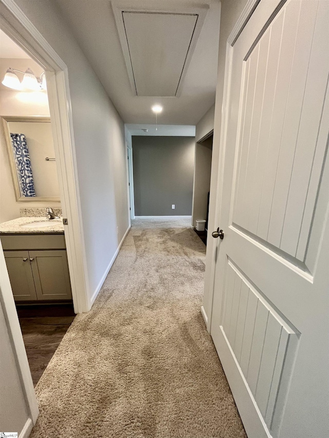 corridor with attic access, dark colored carpet, baseboards, and a sink