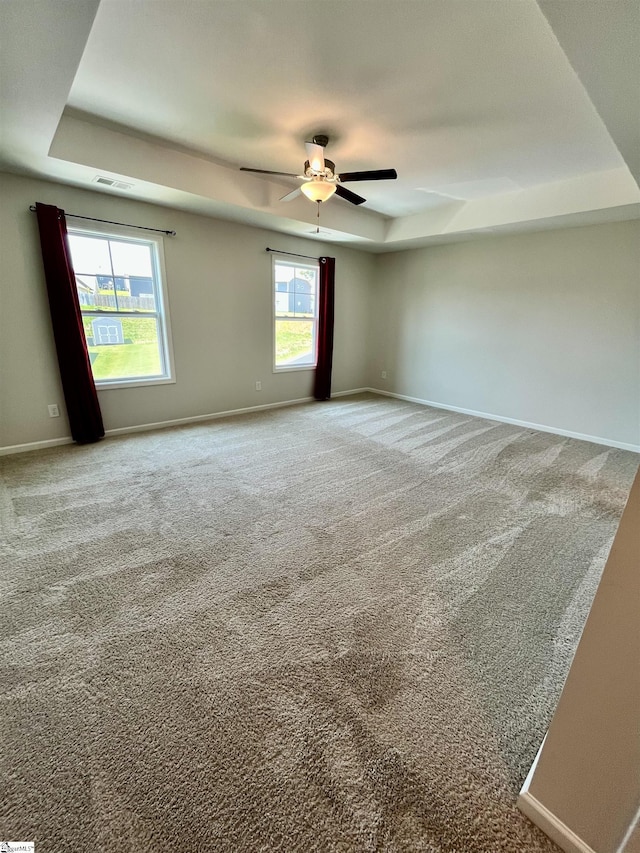 carpeted spare room featuring a tray ceiling, visible vents, baseboards, and ceiling fan