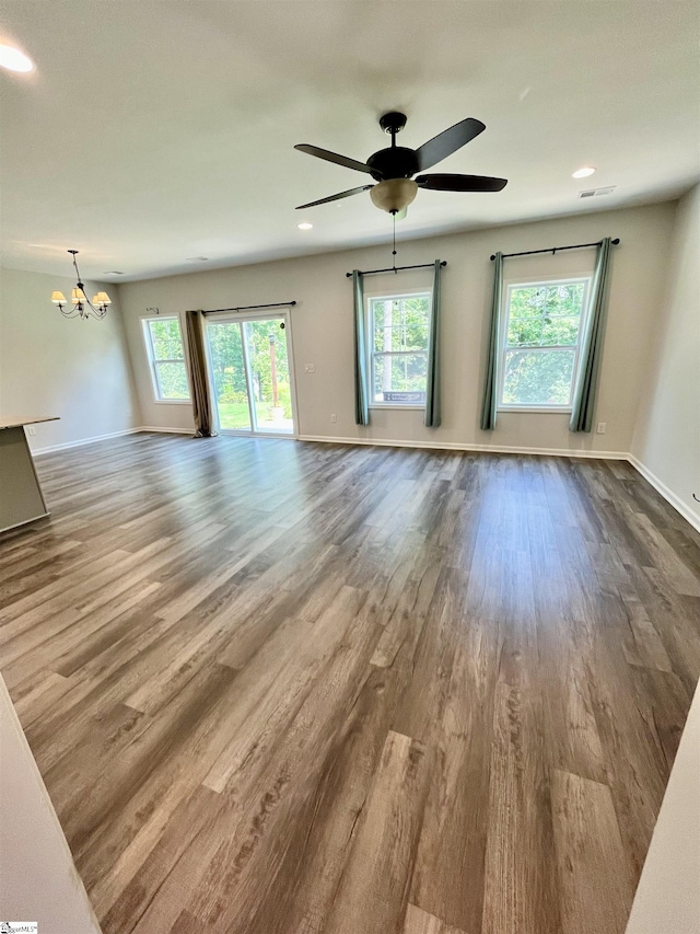 unfurnished living room with dark wood finished floors, plenty of natural light, baseboards, and ceiling fan with notable chandelier