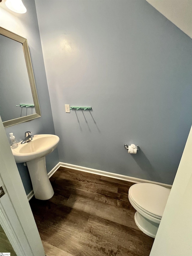 half bathroom with baseboards, wood finished floors, a sink, and toilet