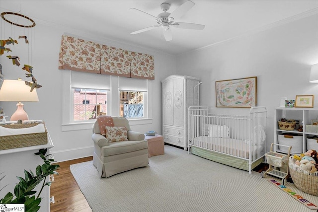 bedroom featuring ceiling fan, wood finished floors, a nursery area, and crown molding
