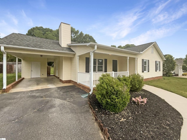 ranch-style house with a chimney, a front lawn, driveway, a porch, and roof with shingles