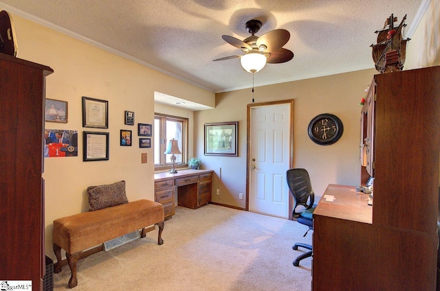 office featuring a textured ceiling, baseboards, light colored carpet, ceiling fan, and ornamental molding