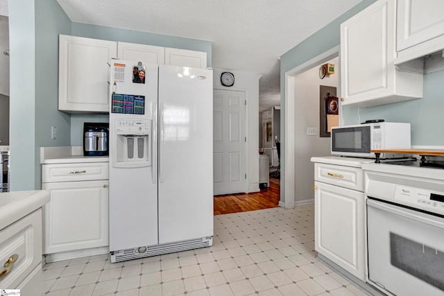 kitchen with white cabinets, a textured ceiling, white appliances, and light countertops