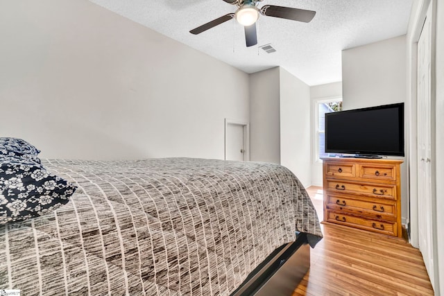 bedroom with ceiling fan, a textured ceiling, visible vents, and light wood-type flooring