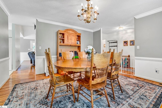 dining space with crown molding, a chandelier, light wood-style floors, and a textured ceiling