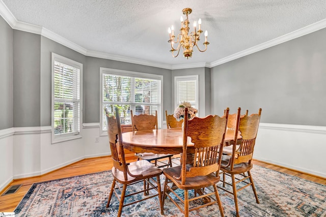 dining space featuring an inviting chandelier, visible vents, ornamental molding, light wood-style flooring, and a textured ceiling