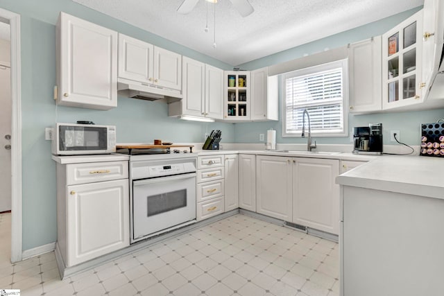kitchen with a sink, white appliances, ceiling fan, white cabinets, and under cabinet range hood