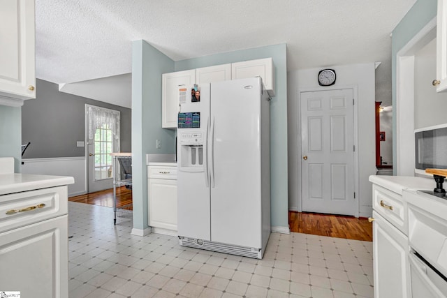 kitchen featuring a wainscoted wall, a textured ceiling, white cabinetry, white refrigerator with ice dispenser, and light countertops